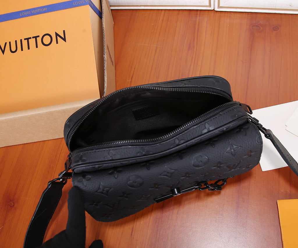 Dark monogram crossbody bag with curved top zip and crossbody strap on wood surface