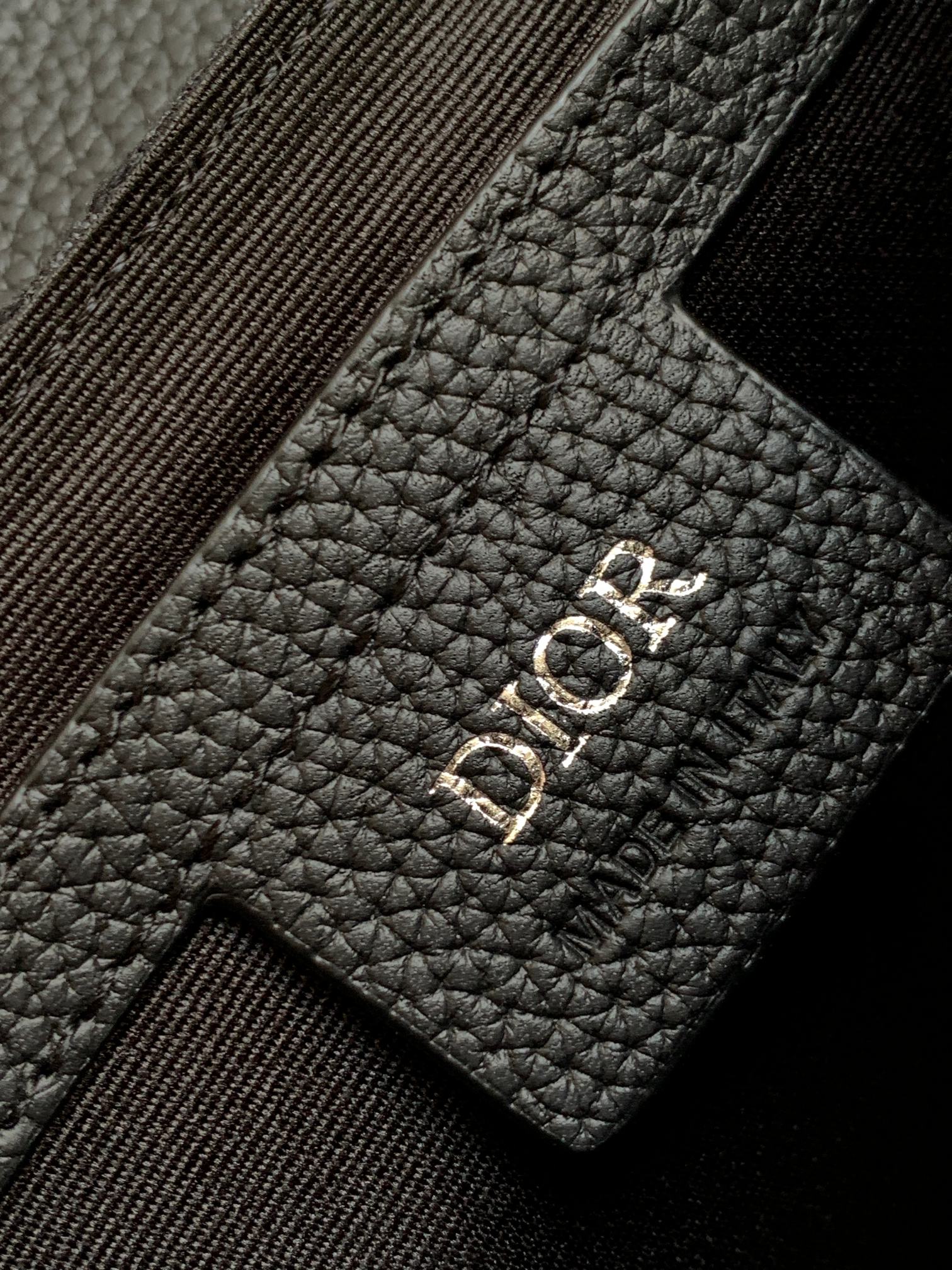 Dior bag detail, black leather patch with Dior logo and stitched strap edge