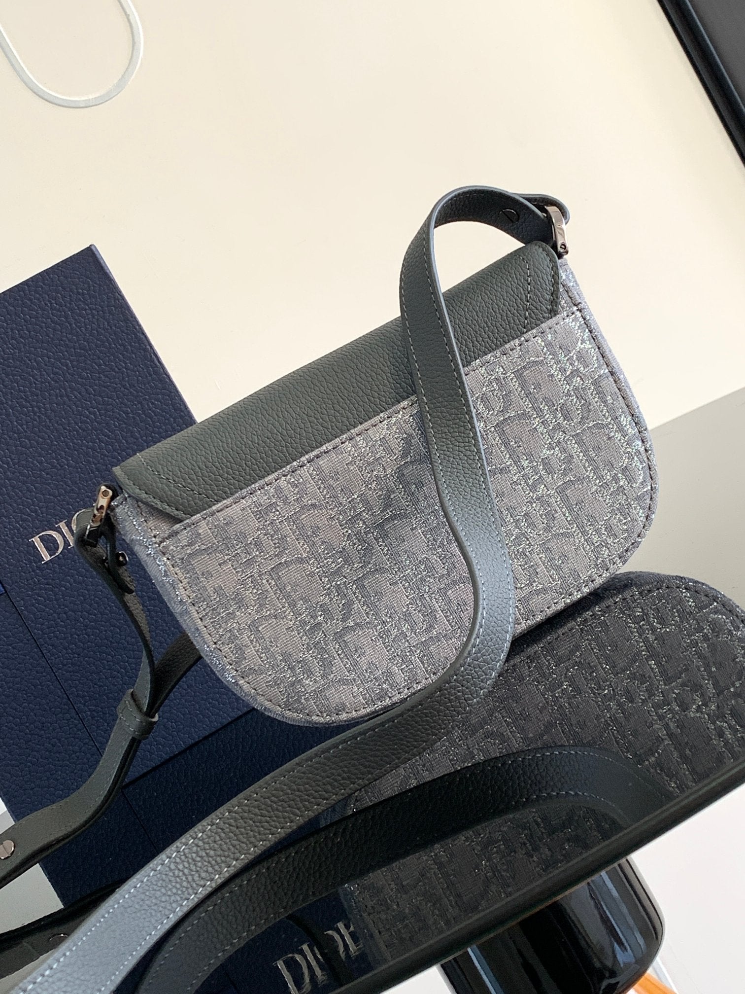Dior gray small bag with curved flap, patterned body, and side strap detail.