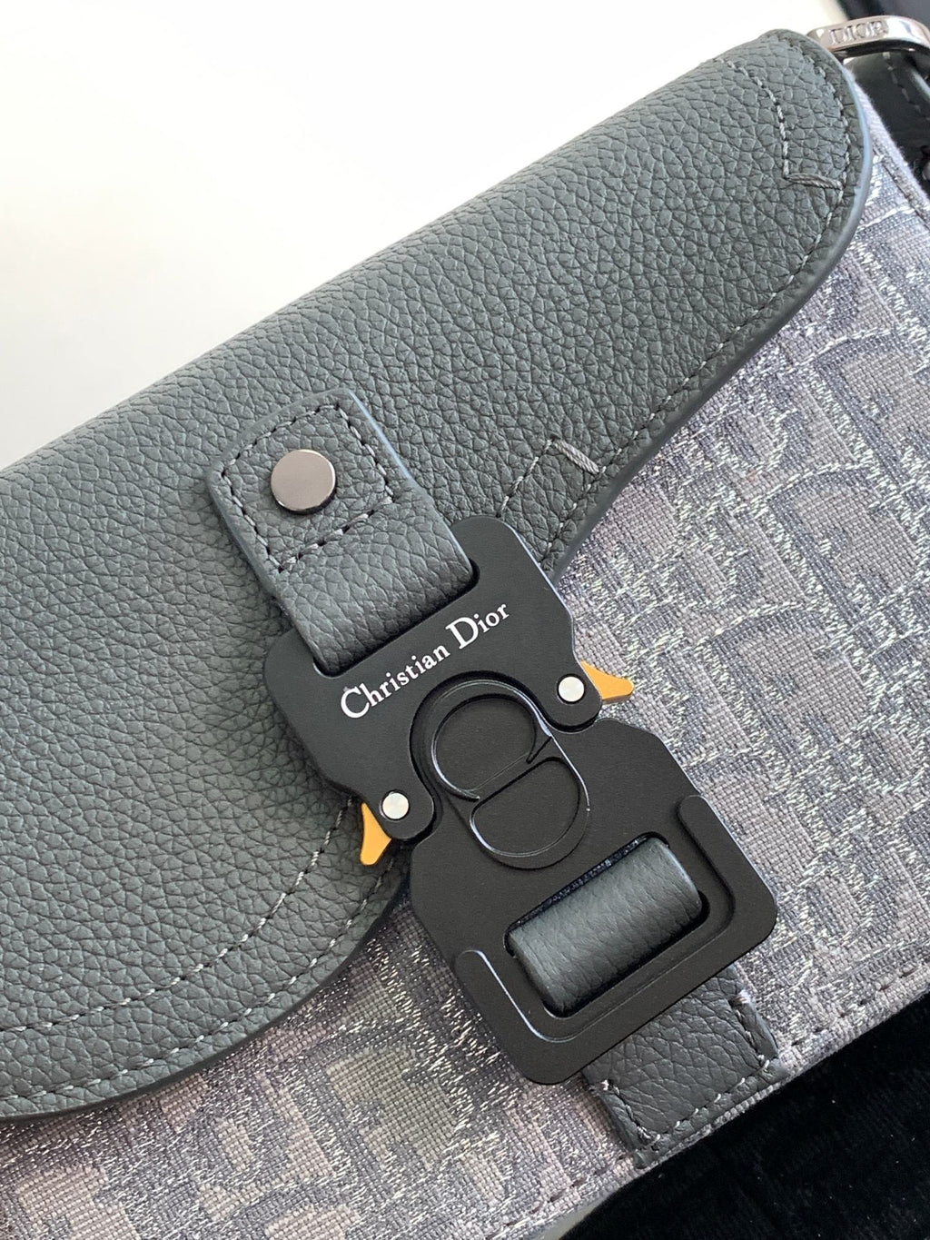 Dior gray leather bag with snap flap, black logo charm, and patterned panel.