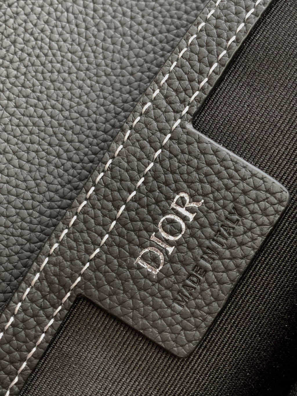 Dior logo leather patch on a dark textured bag, with white contrast stitching