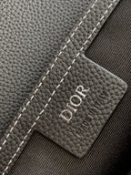 Dior logo leather patch on a dark textured bag, with white contrast stitching