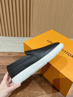 Black leather slip-on sneakers with white sole, held by hand