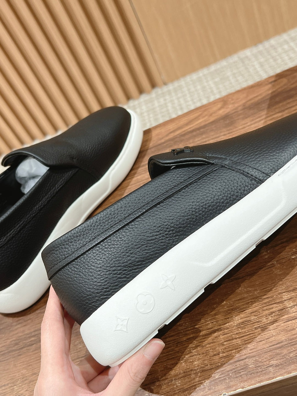 Black leather slip-on sneakers with white soles, held side by side