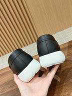 Black leather slip-on sneakers with white soles, heel view in hand