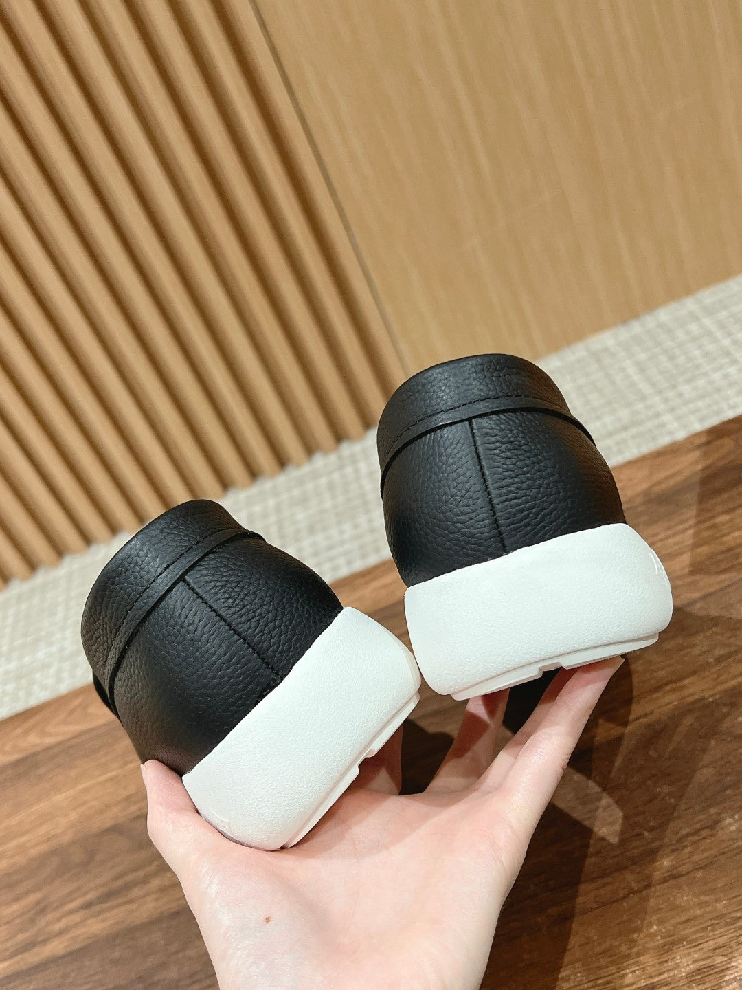 Black leather slip-on sneakers with white soles, heel view in hand