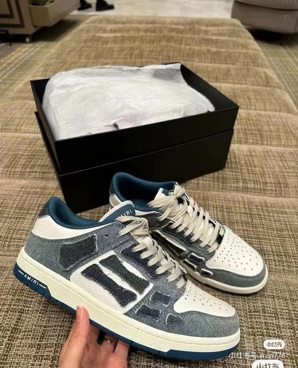 Amiri low-top sneakers on sofa, gray and white uppers with blue logo detailing