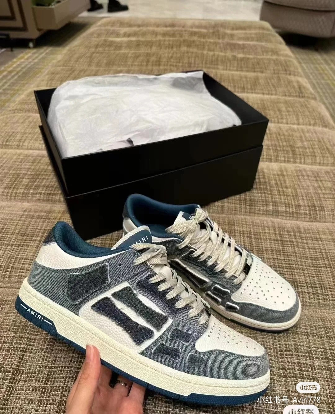Amiri low-top sneakers on sofa, gray and white uppers with blue logo detailing