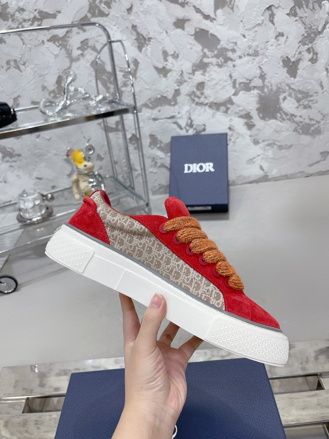 Red suede sneaker with tan rope laces, white sole, held in hand