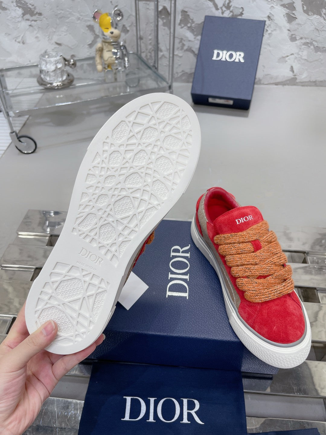 Red suede sneaker outsole with white tread, tan rope laces, Dior logo