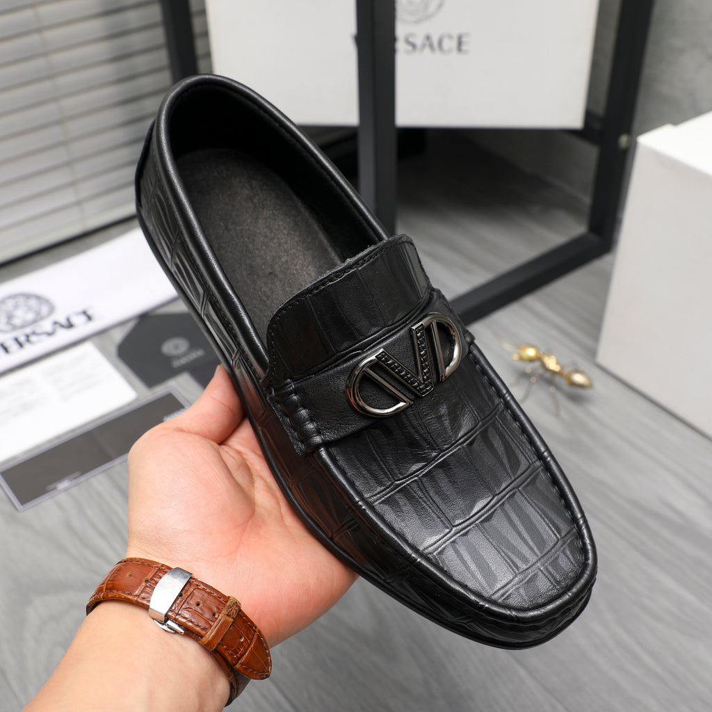 Black leather loafer with embossed texture and metal buckle, worn on hand