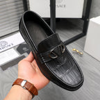 Black leather loafer with embossed texture and metal buckle, worn on hand