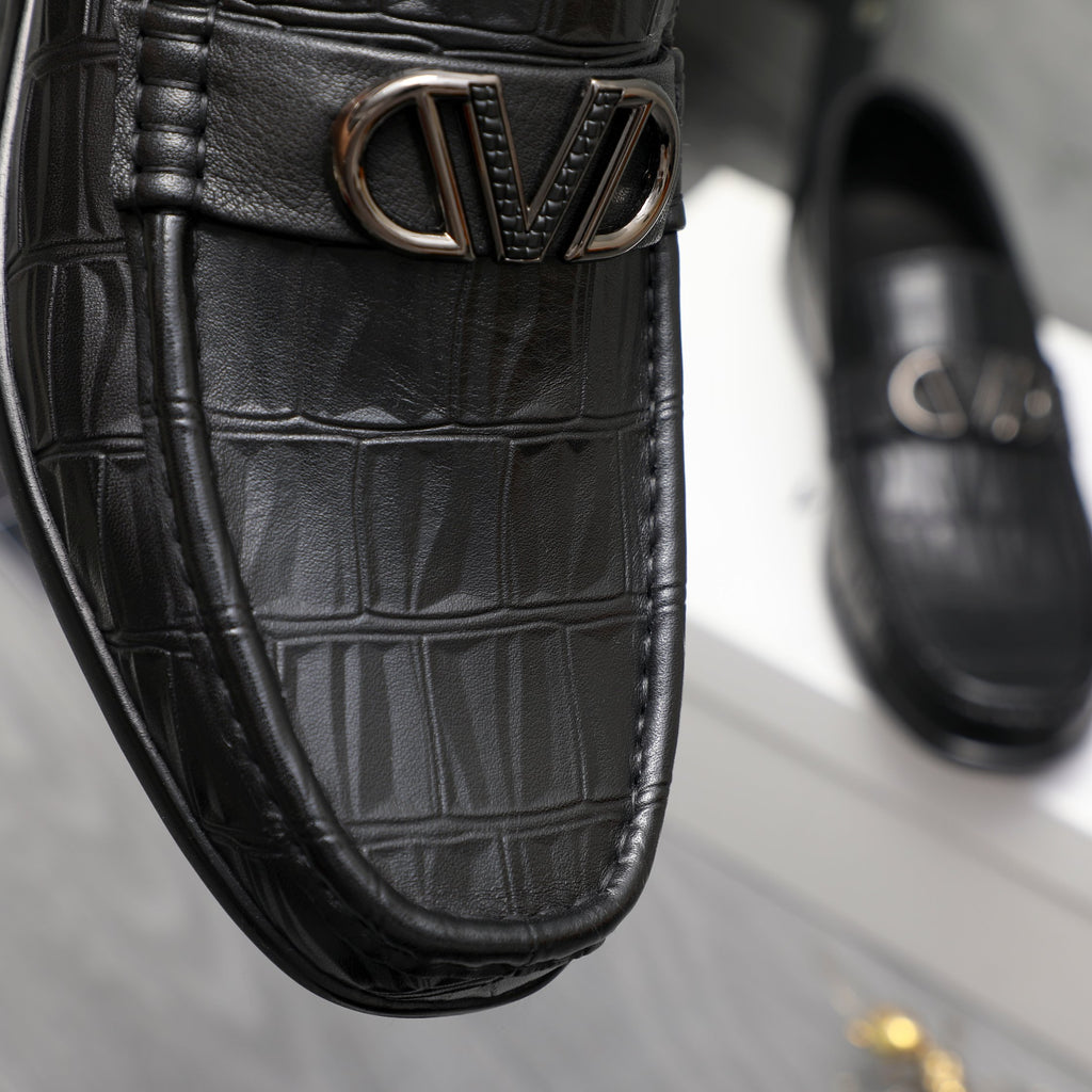 Close-up of black embossed leather loafer with V-shaped metal buckle