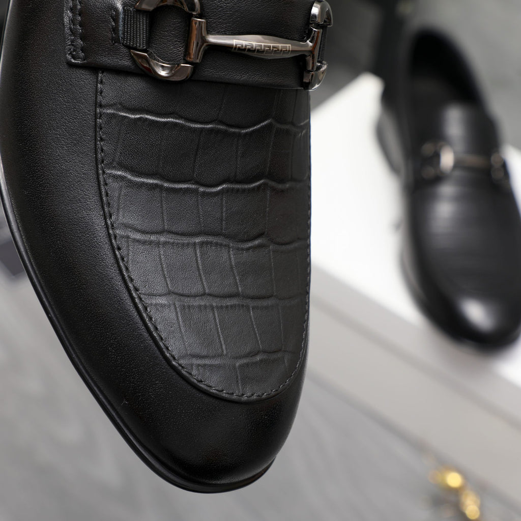 Black leather loafer close-up with croc-embossed paneling and buckle strap