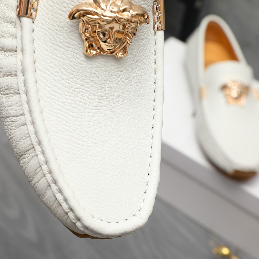 Close-up of white leather loafer with gold bar and ornate emblem on vamp