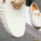Close-up of white leather loafer with gold bar and ornate emblem on vamp