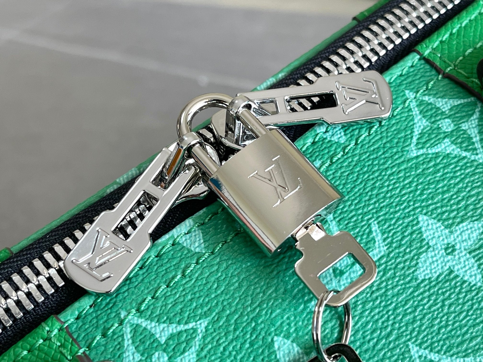 Green Louis Vuitton handbag zipper pull with LV logo and metal hardware.