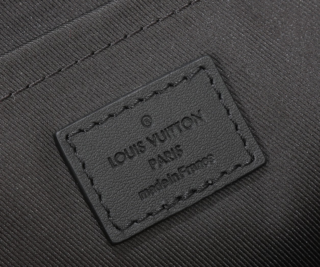 Black leather crossbody bag label patch with embossed Louis Vuitton text