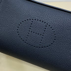 Hermes bag close-up of dark blue pebbled leather with stitched logo motif.