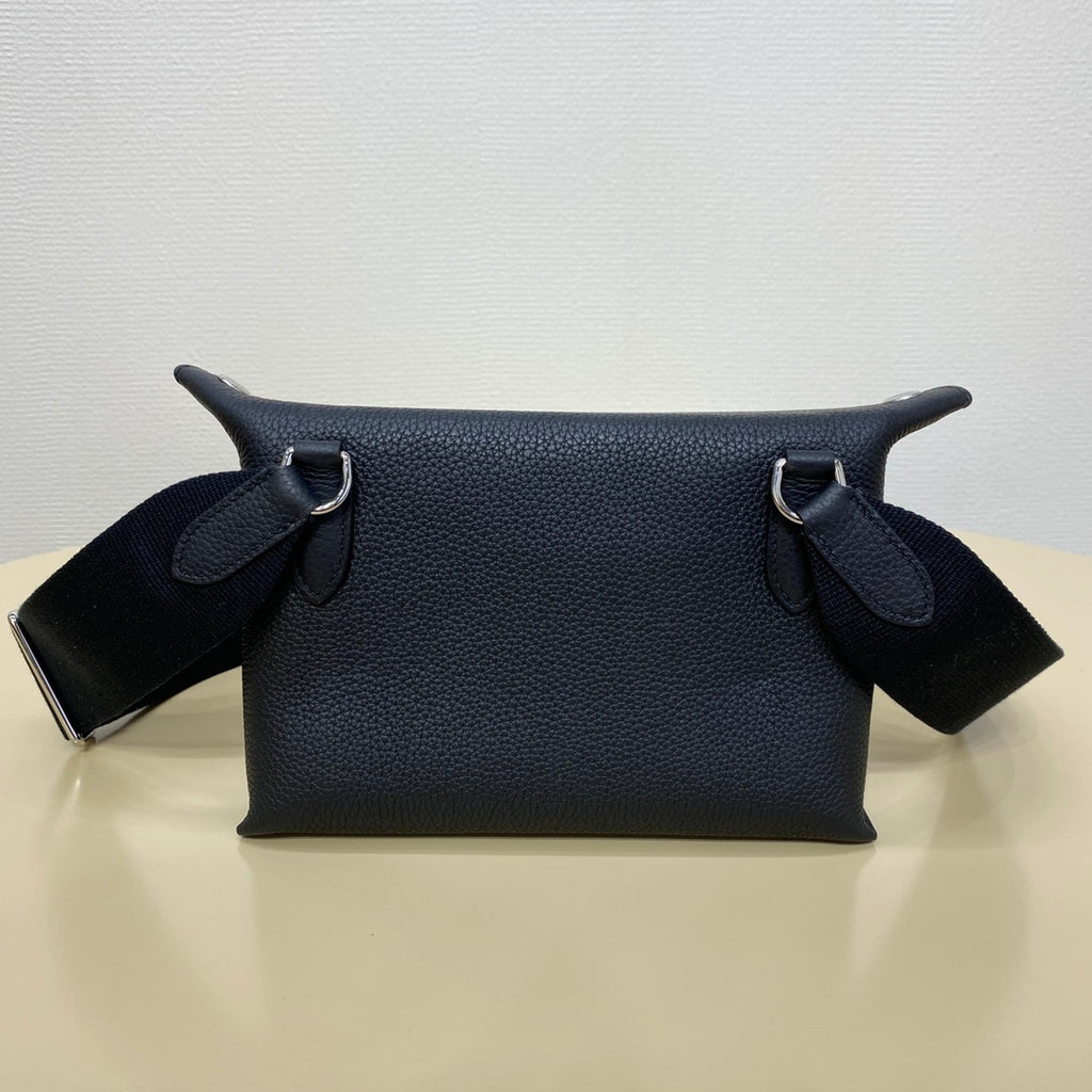Hermes crossbody bag with dark blue leather body, top straps, and metal rings.