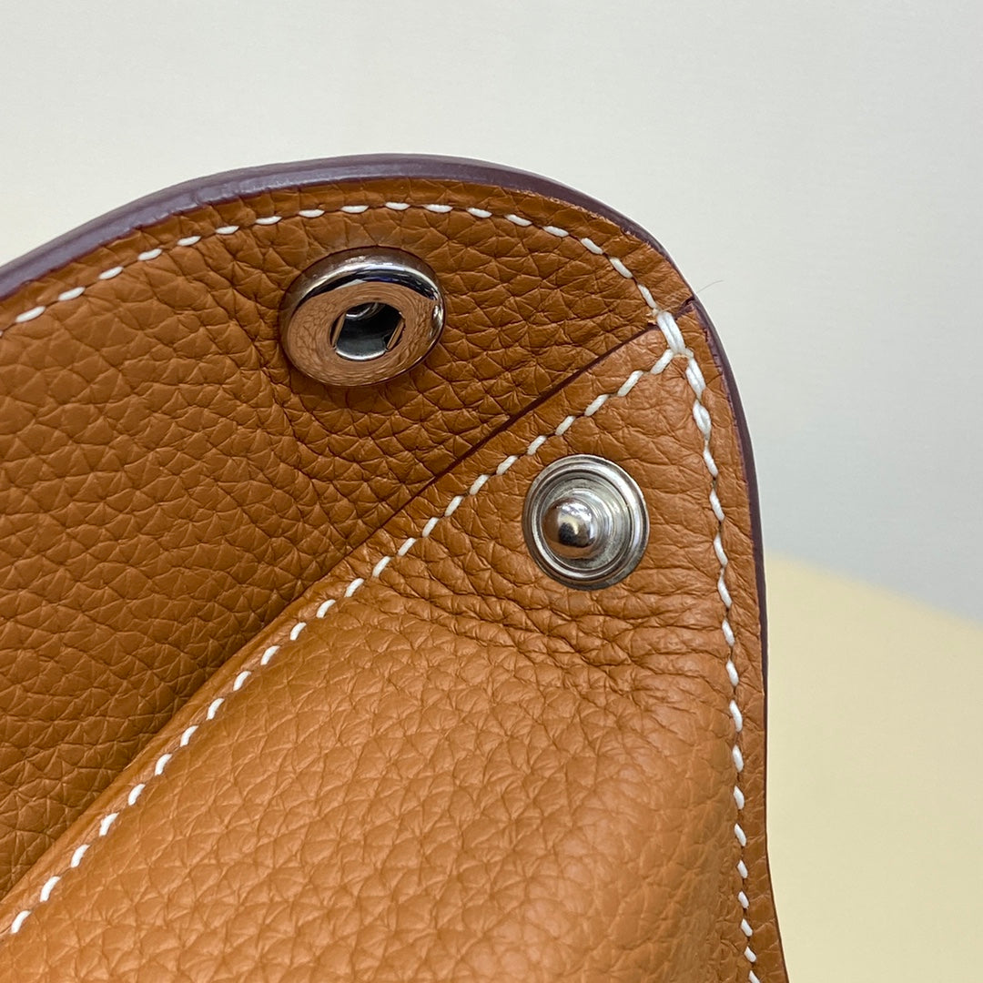 Hermes bag hardware close-up with metal snap and white edge stitching on tan leather