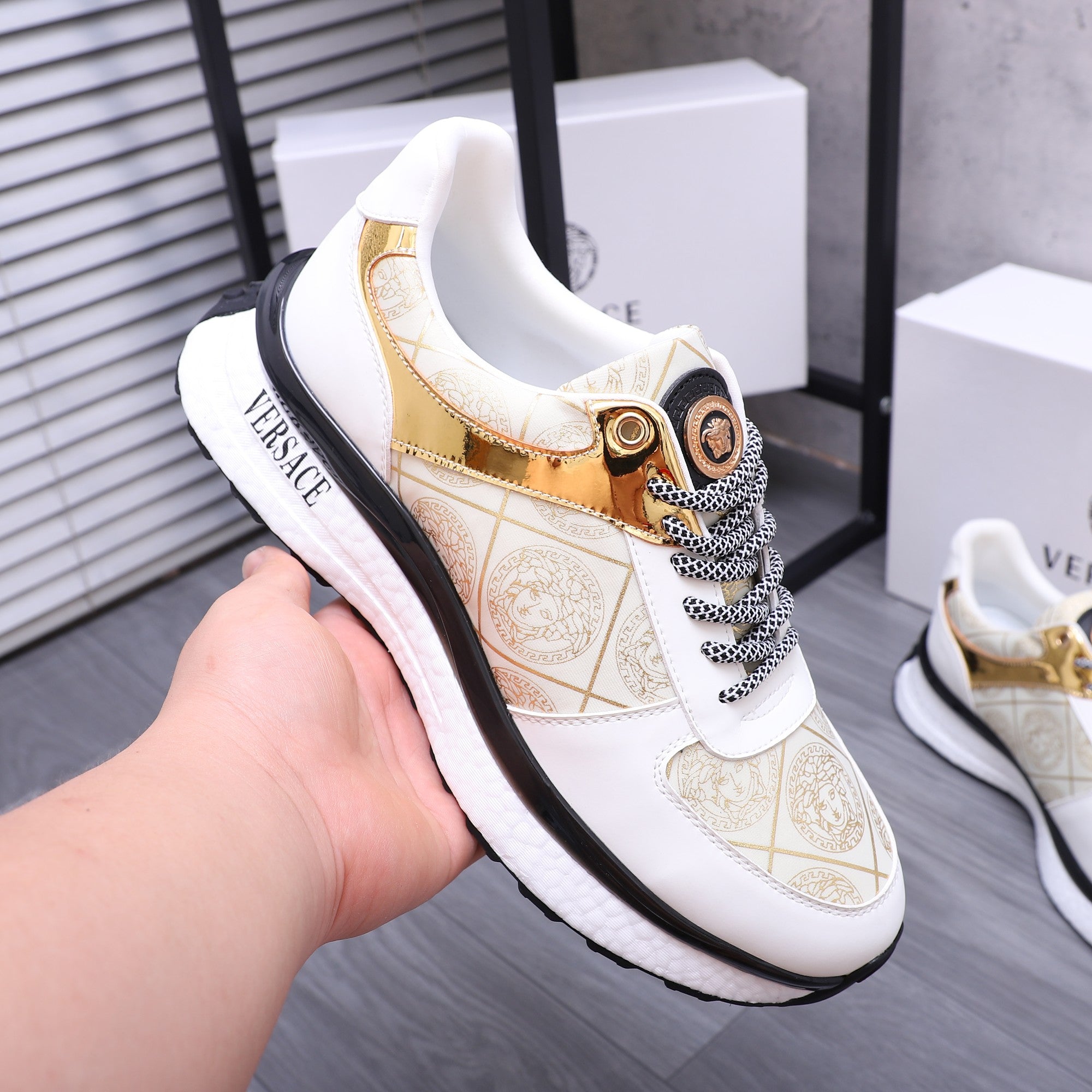 Versace sneakers held in hand: white leather-look upper with gold accents and black trim