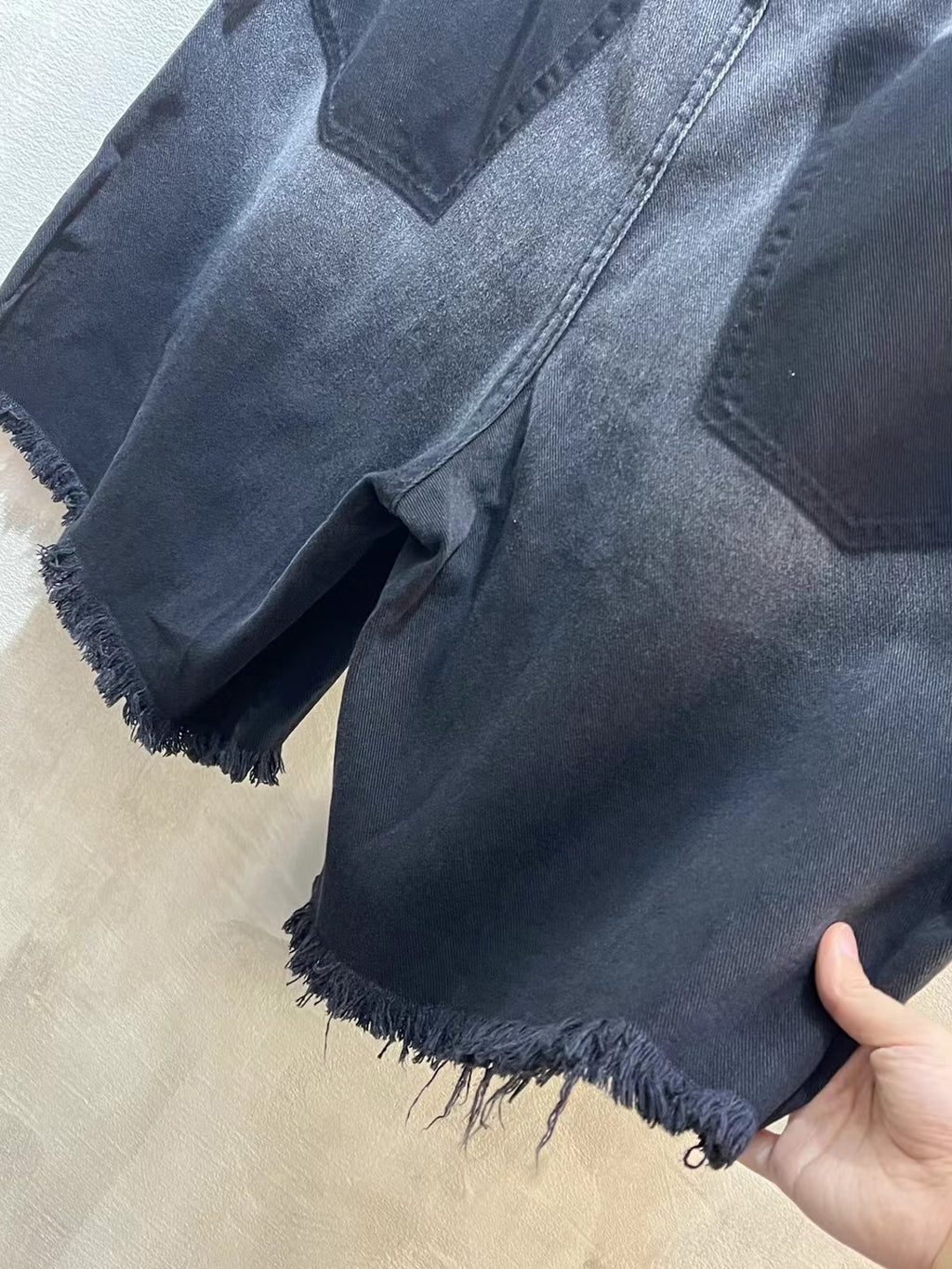 Balenciaga denim shorts, light-to-mid blue wash, distressed frayed hem, hand holding