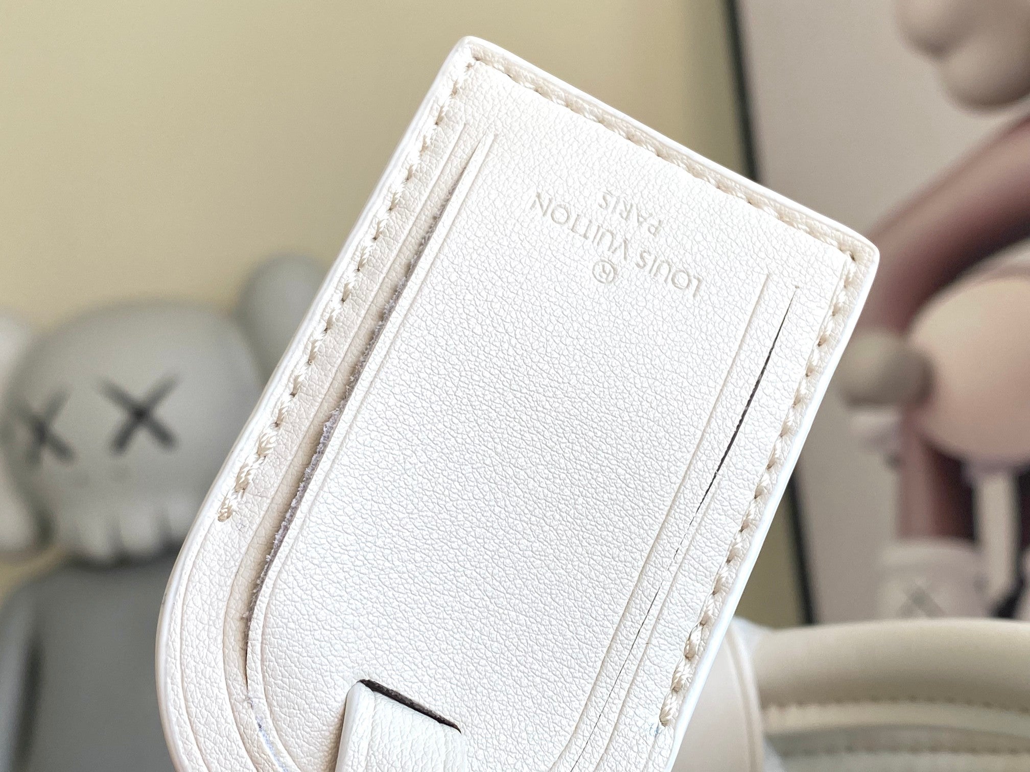 White leather duffel bag strap tab with stitched edges and embossed logo lettering