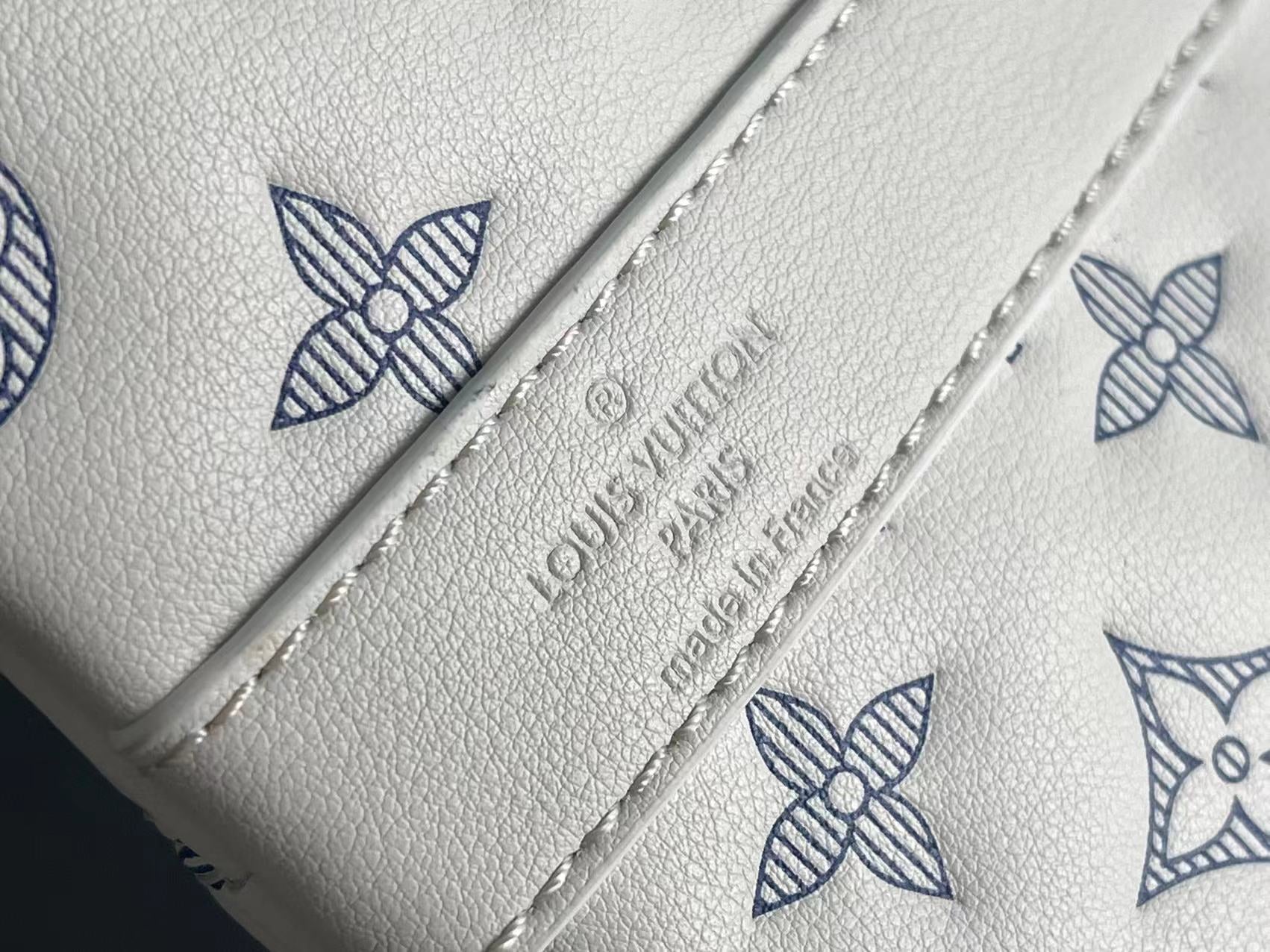 Close-up of white leather panel with blue monogram print and embossed logo lettering