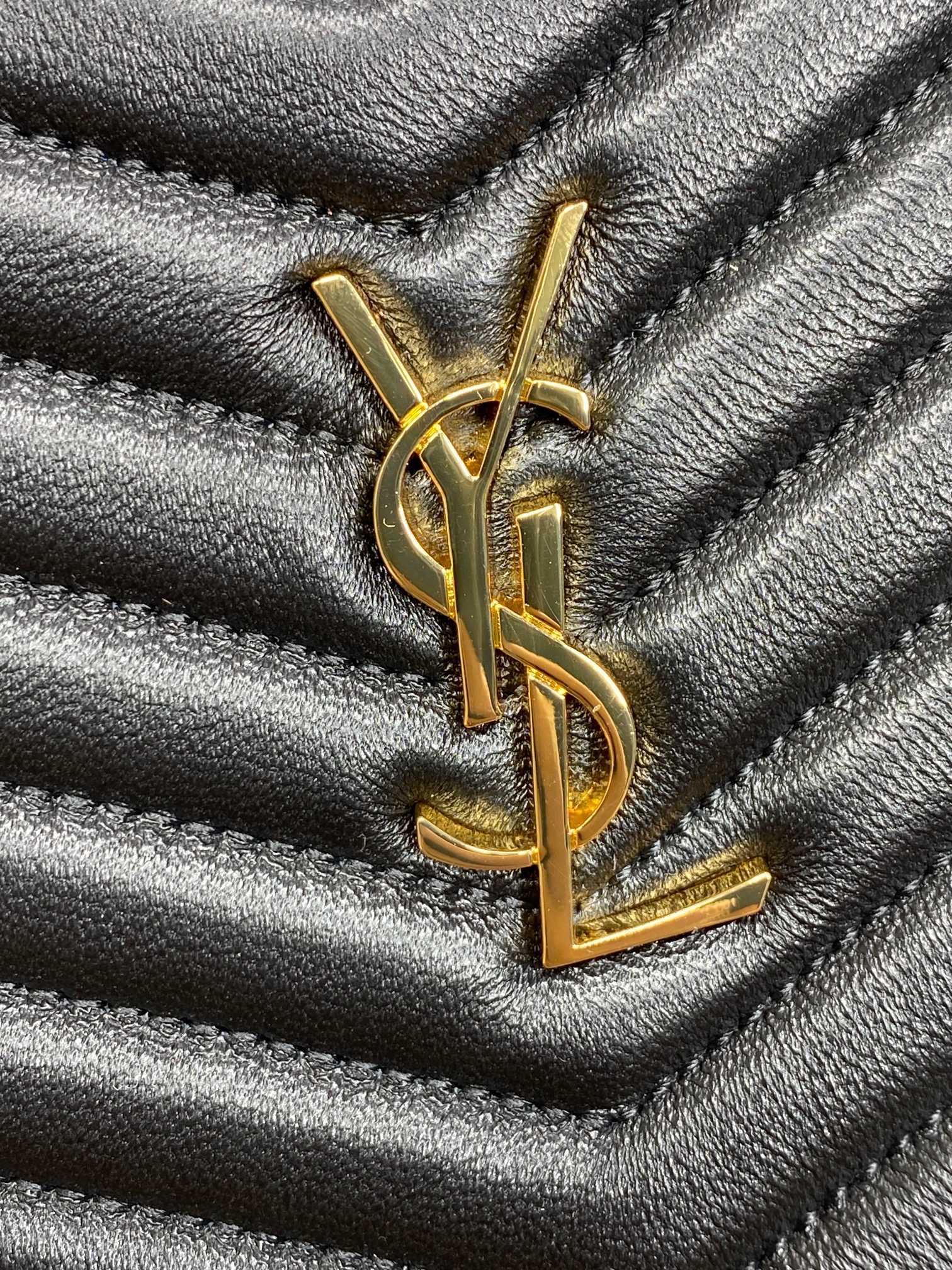 Close-up of YSL logo on black quilted bag with gold-tone metal hardware