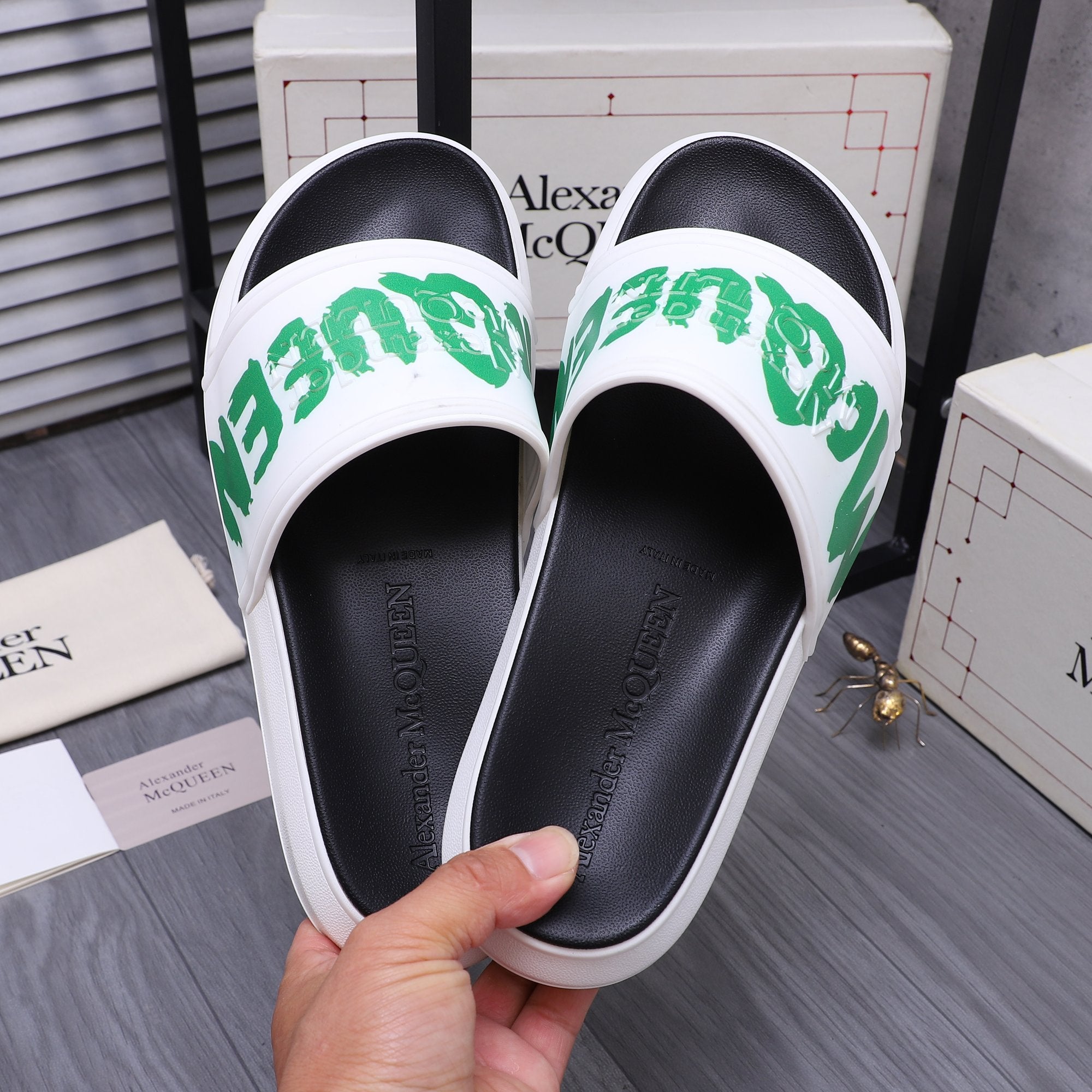 Black slide sandal with white strap and green logo, held in hand