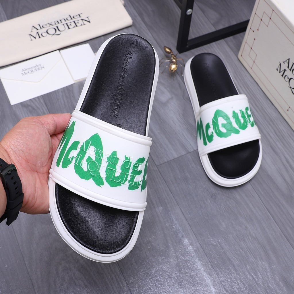 Black slide sandal with white strap and green logo lettering, shown in hand