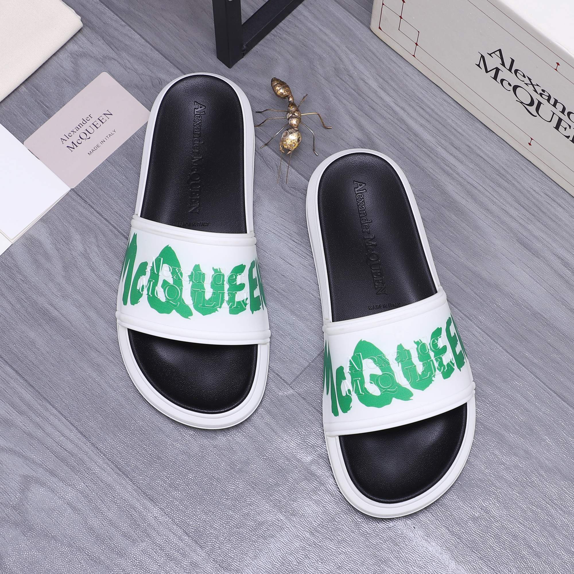 Black and white slide sandals with green logo on the front strap