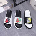 Slide sandals with white straps and colorful graphic print, black footbeds.