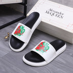 Slide sandal pair with white straps and red/green graphic emblem on black uppers.