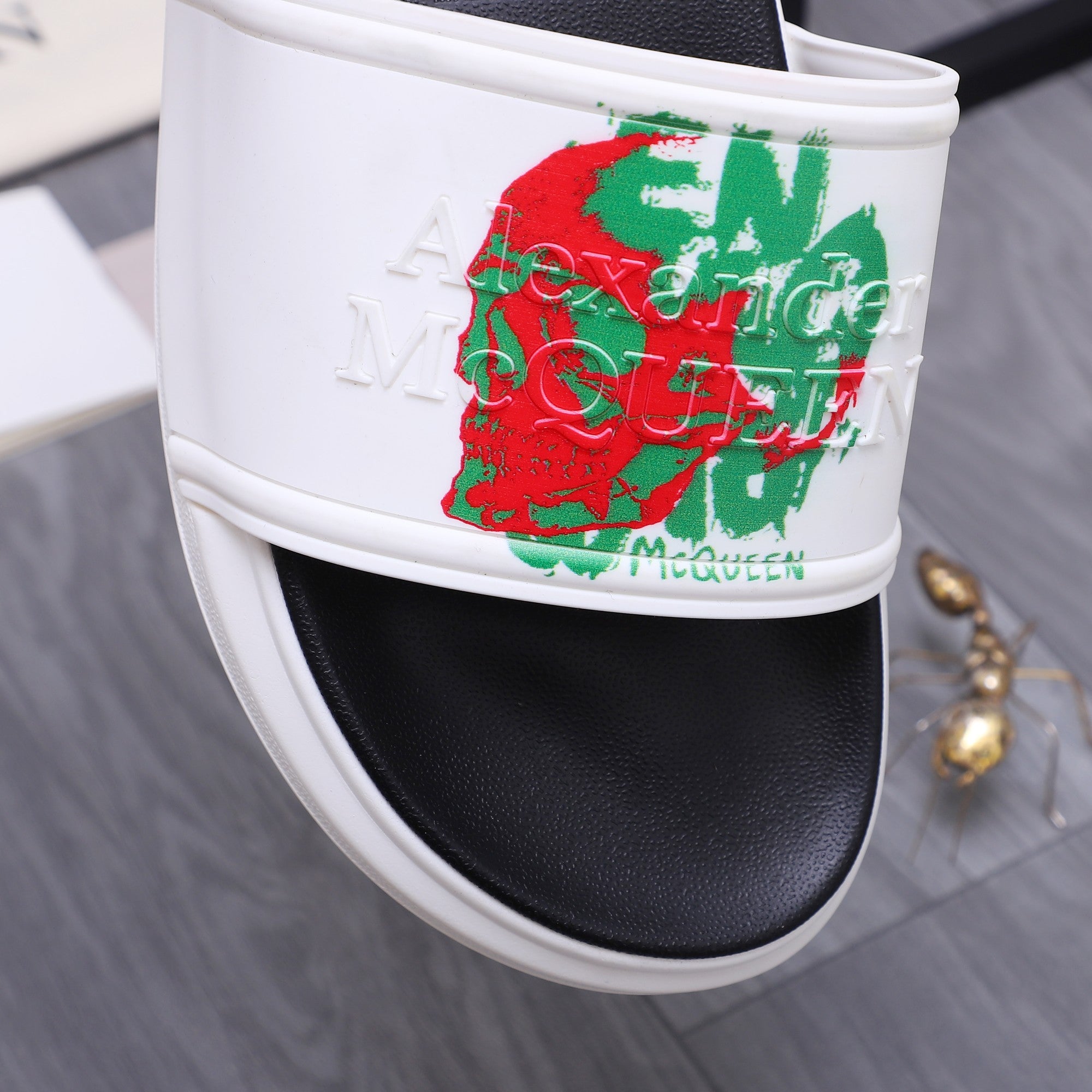 White slide strap with red and green graphic emblem over black underfoot.