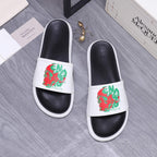 Slide sandals with white straps featuring red and green graphic print on black leather.