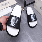 Hand holding black slide sandal; white footbed and white portrait print on strap.