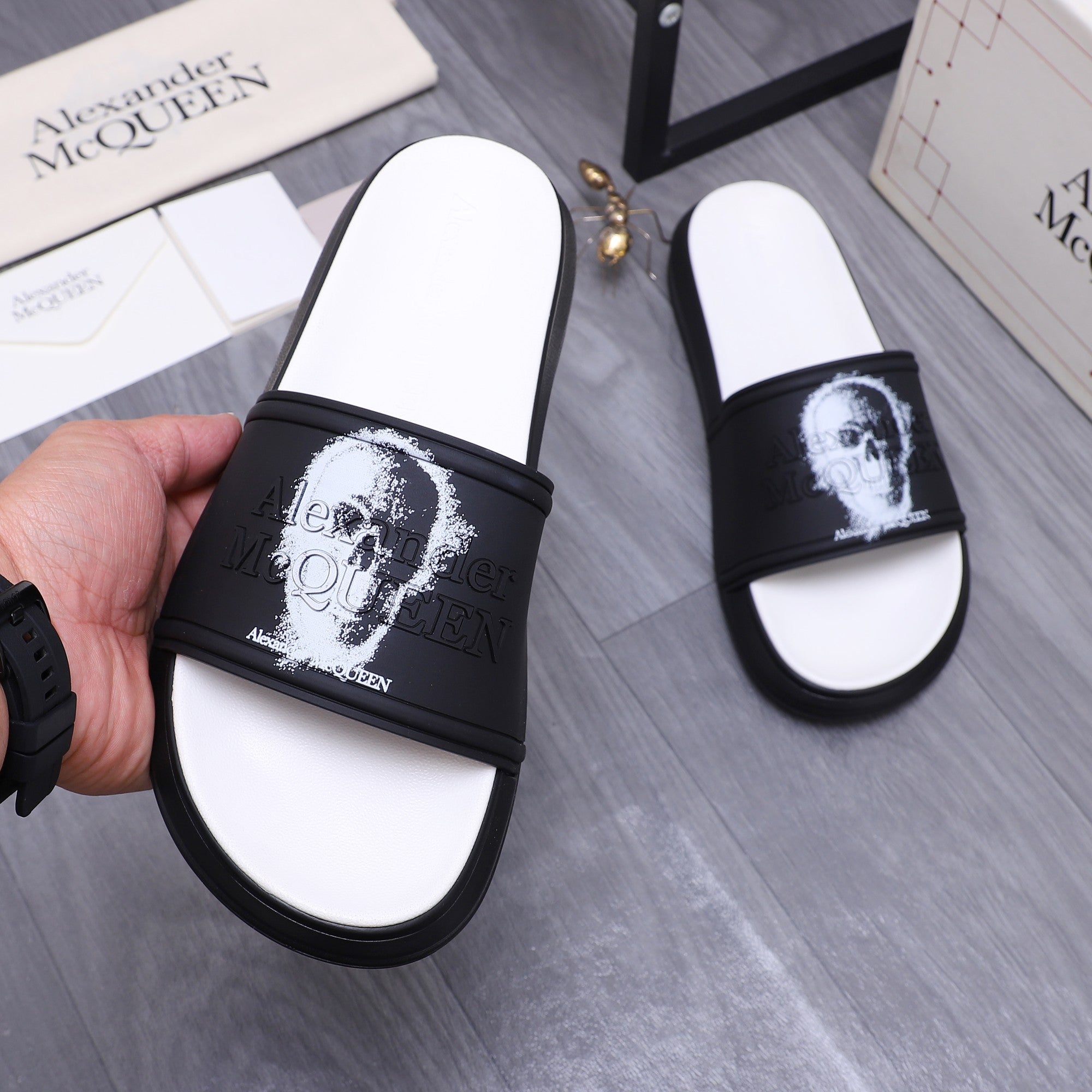 Hand holding black slide sandal; white footbed and white portrait print on strap.