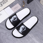 Pair of black slide sandals with white footbeds and white portrait graphic on straps.