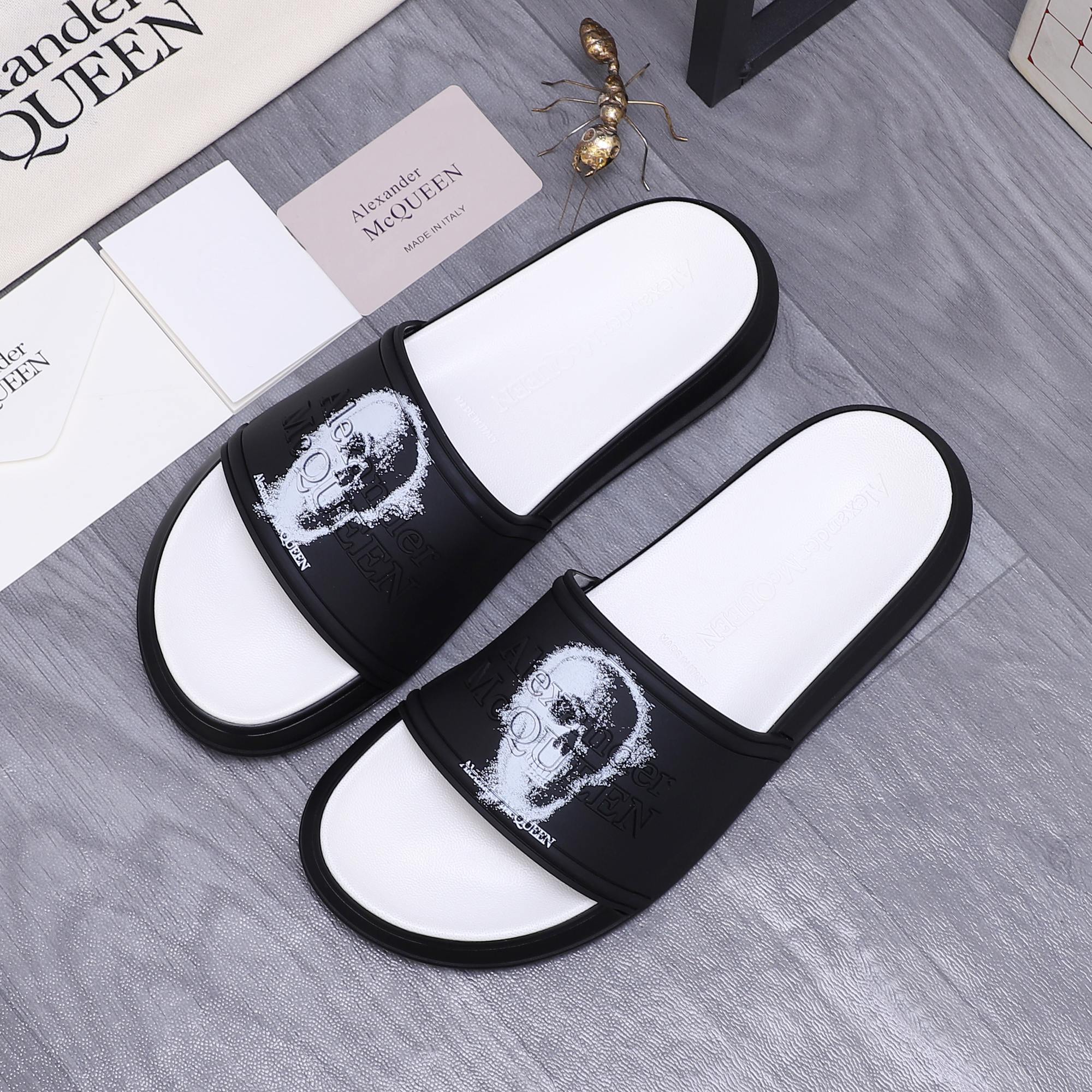 Pair of black slide sandals with white footbeds and white portrait graphic on straps.