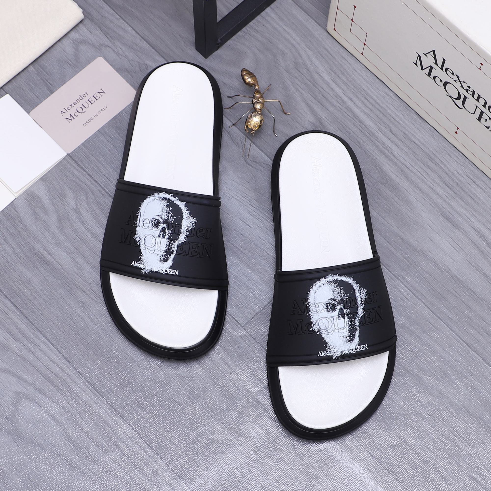 Two black-and-white slide sandals with white portrait print on straps, rounded toe.