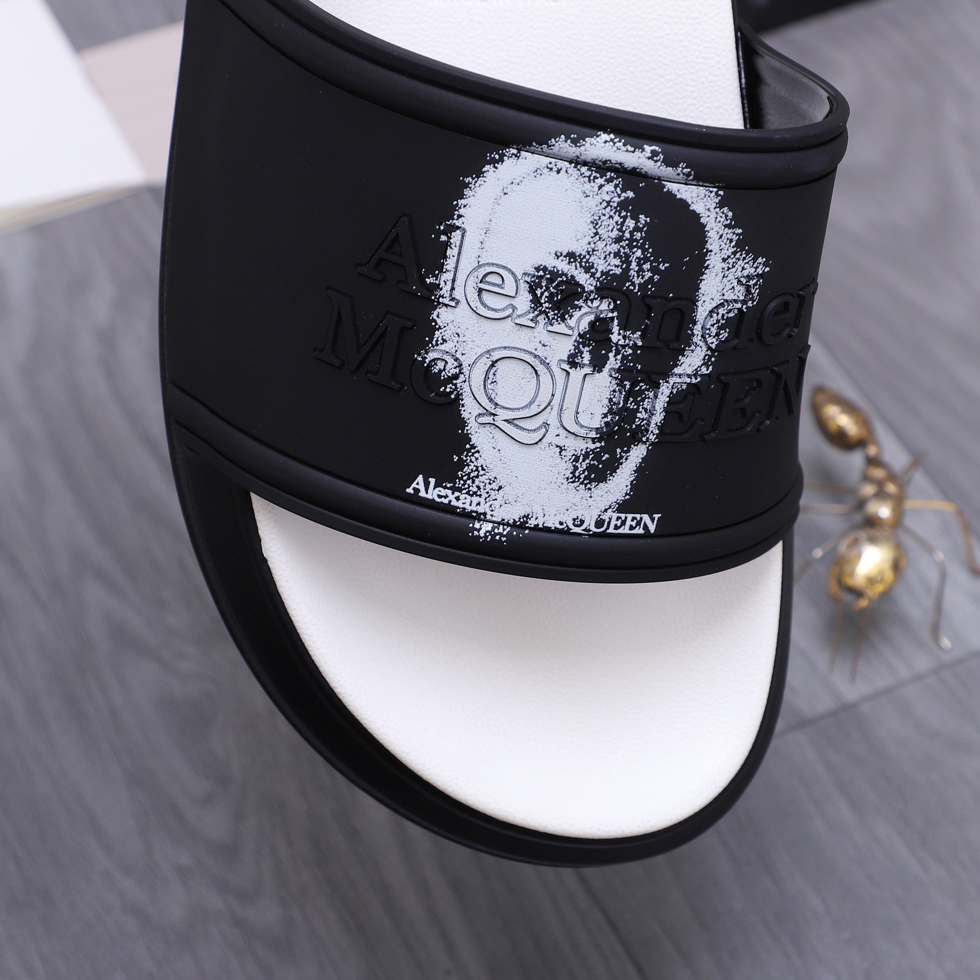 Close-up of black slide sandal strap with white portrait print and small logo text.
