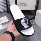 Black slide sandal held in hand; strap has white portrait graphic on black band.