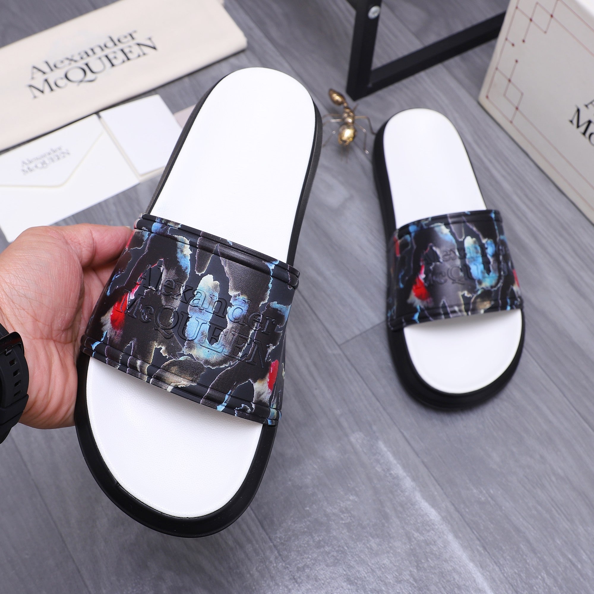 Hand holding black slide sandals with white footbeds and colorful printed straps