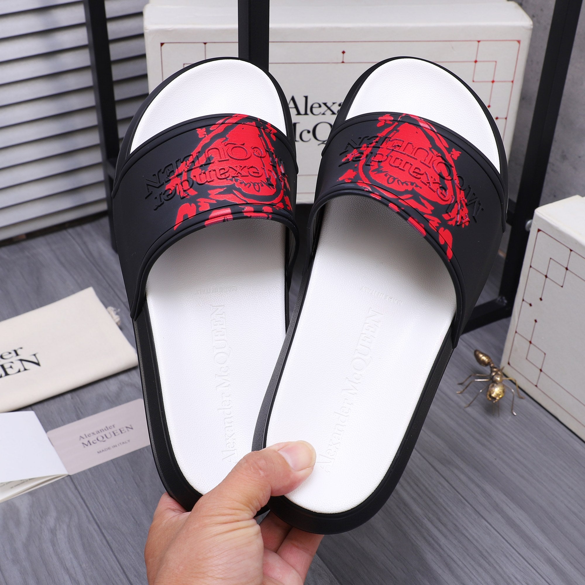 Black slide sandals with red graphic strap and white footbed, close-up view