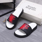 Black slide sandals with red patterned strap and white footbed with curved edges