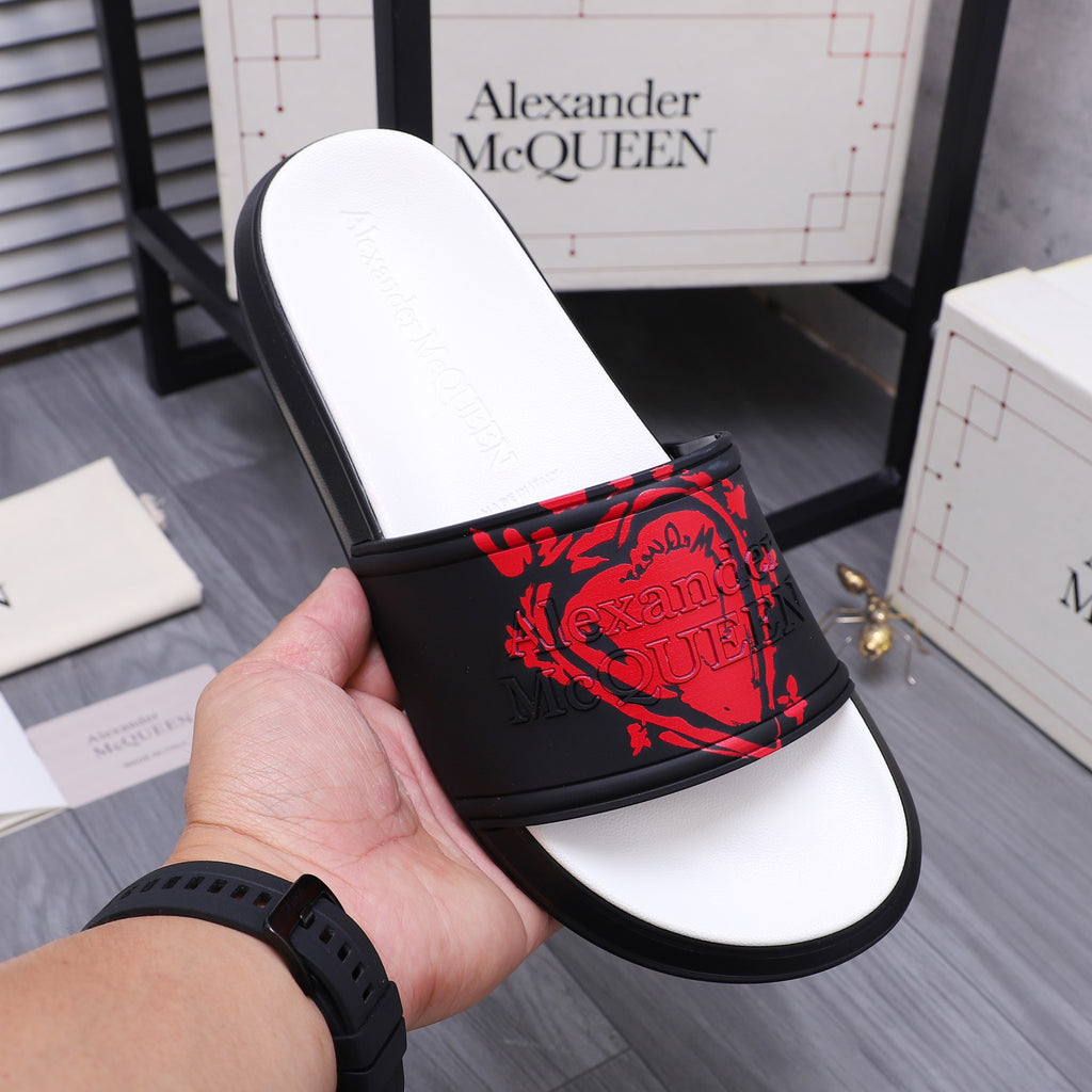 Black slide sandal with red graphic strap and white footbed, hand holding the shoe