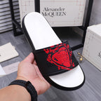 Black slide sandal with red graphic strap and white footbed, hand holding the shoe