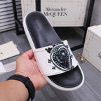 Alexander McQueen slide sandals, white strap with black crest graphic, in hand view